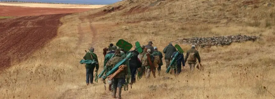 Estate staff walking out along a farm track at El Crespo carrying peg markers, shooting sticks and cartridge bags