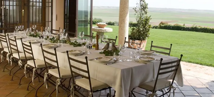 A long table laid for lunch under a covered terrace at El Crespo, looking out across lawns to open farmland
