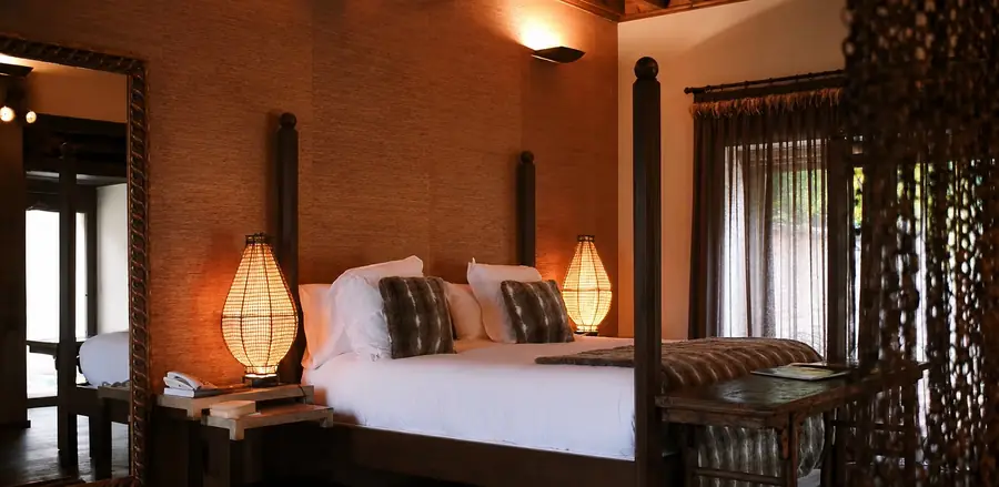 A bedroom at El Despenadero with a dark four-poster bed, grasscloth walls and woven lantern lamps