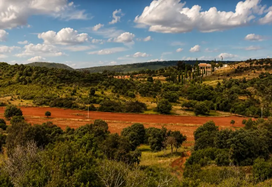 Red ploughed fields and holm oak pasture at El Despenadero, a white farmhouse on the ridge beyond